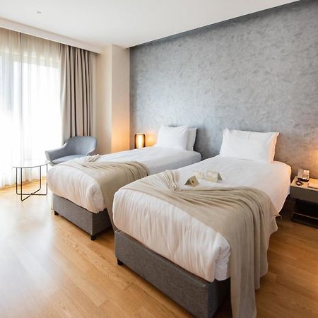 Dosso Dossi Hotels & Spa Downtown Istanbul Ngoại thất bức ảnh The photo shows a modern hotel room featuring two single beds with white linens and soft gray throw blankets. The room has a stylish design, with wooden flooring and a large window dressed with light curtains that allow natural light to enter. There'