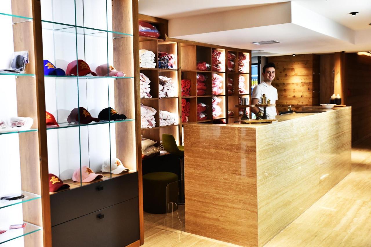 Dosso Dossi Hotels & Spa Downtown Istanbul Ngoại thất bức ảnh The photo shows a retail space or reception area with a warm and modern design. On the left, there are shelves displaying various colorful caps, neatly arranged behind glass. The right side features a wooden counter where a staff member is standing, 