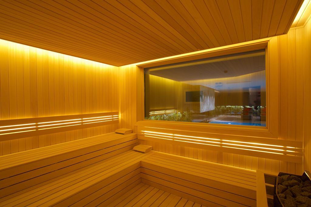 Dosso Dossi Hotels & Spa Downtown Istanbul Ngoại thất bức ảnh The photo depicts a sauna interior characterized by wooden paneling and warm, ambient lighting. The walls and seating are made of light-colored wood, creating a cozy atmosphere. There is a large window that offers a view into another room, possibly f