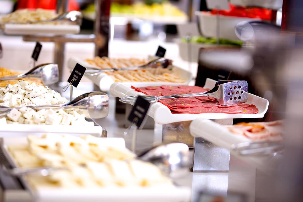 Dosso Dossi Hotels & Spa Downtown Istanbul Ngoại thất bức ảnh The image displays a buffet setting with various food items arranged on tables. There are multiple white serving trays filled with different types of food, including sliced meats, spreads, and possibly salads or other accompaniments. Each tray has a 