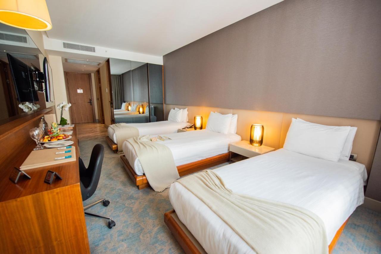 Dosso Dossi Hotels & Spa Downtown Istanbul Ngoại thất bức ảnh The photo shows a modern hotel room featuring two single beds, each with white linens and a light blanket partially draped over them. There are stylish bedside lamps on either side of the beds, providing a warm glow. A wooden desk and chair are posit
