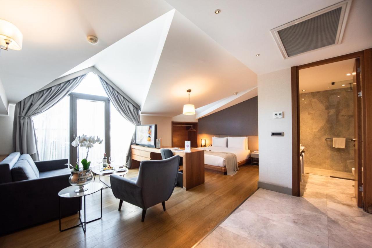 Dosso Dossi Hotels & Spa Downtown Istanbul Ngoại thất bức ảnh The photo shows a stylish hotel room with a modern design. It features slanted ceilings and large windows that allow natural light to flood the space. The room includes a comfortable seating area with a sofa and a small table, as well as a well-made 