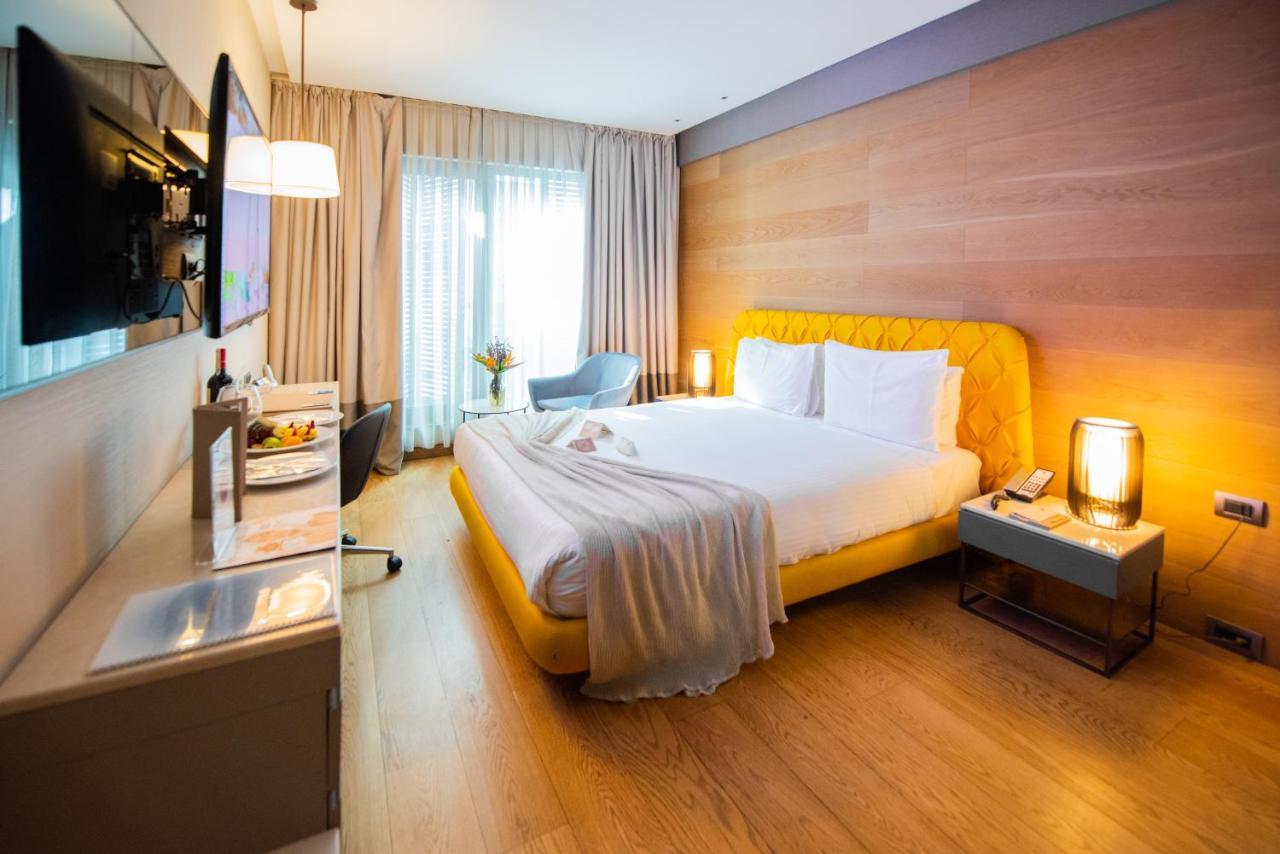 Dosso Dossi Hotels & Spa Downtown Istanbul Ngoại thất bức ảnh The photo shows a modern hotel room with a cozy and inviting atmosphere. The room features a large bed with a yellow upholstered headboard, topped with white bedding and a soft gray throw blanket casually draped over it. To the side of the bed is a s