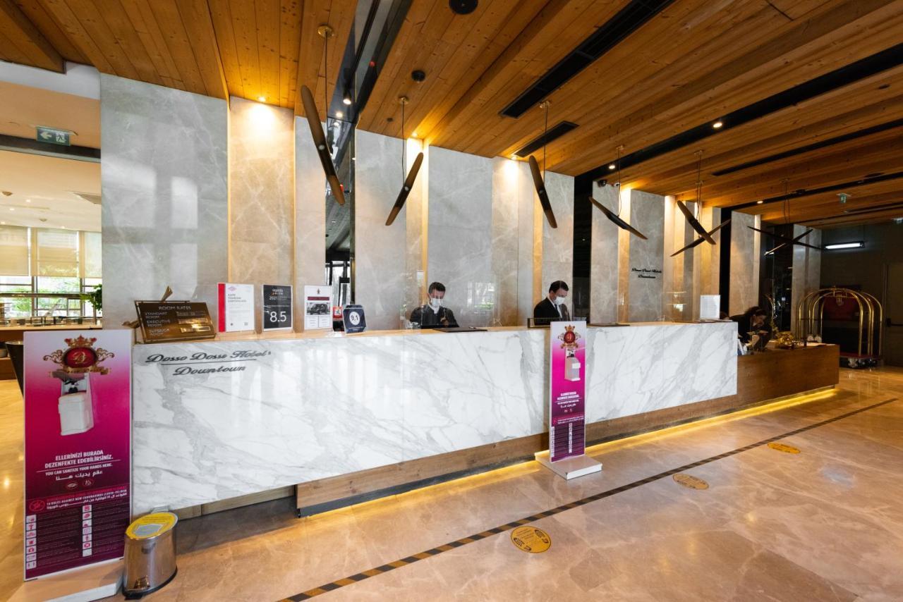 Dosso Dossi Hotels & Spa Downtown Istanbul Ngoại thất bức ảnh The photo shows a hotel reception area. The front desk is made of elegant marble, and the space features wooden accents on the ceiling. Behind the counter, two staff members are visible, likely assisting guests. There are signs and promotional materi