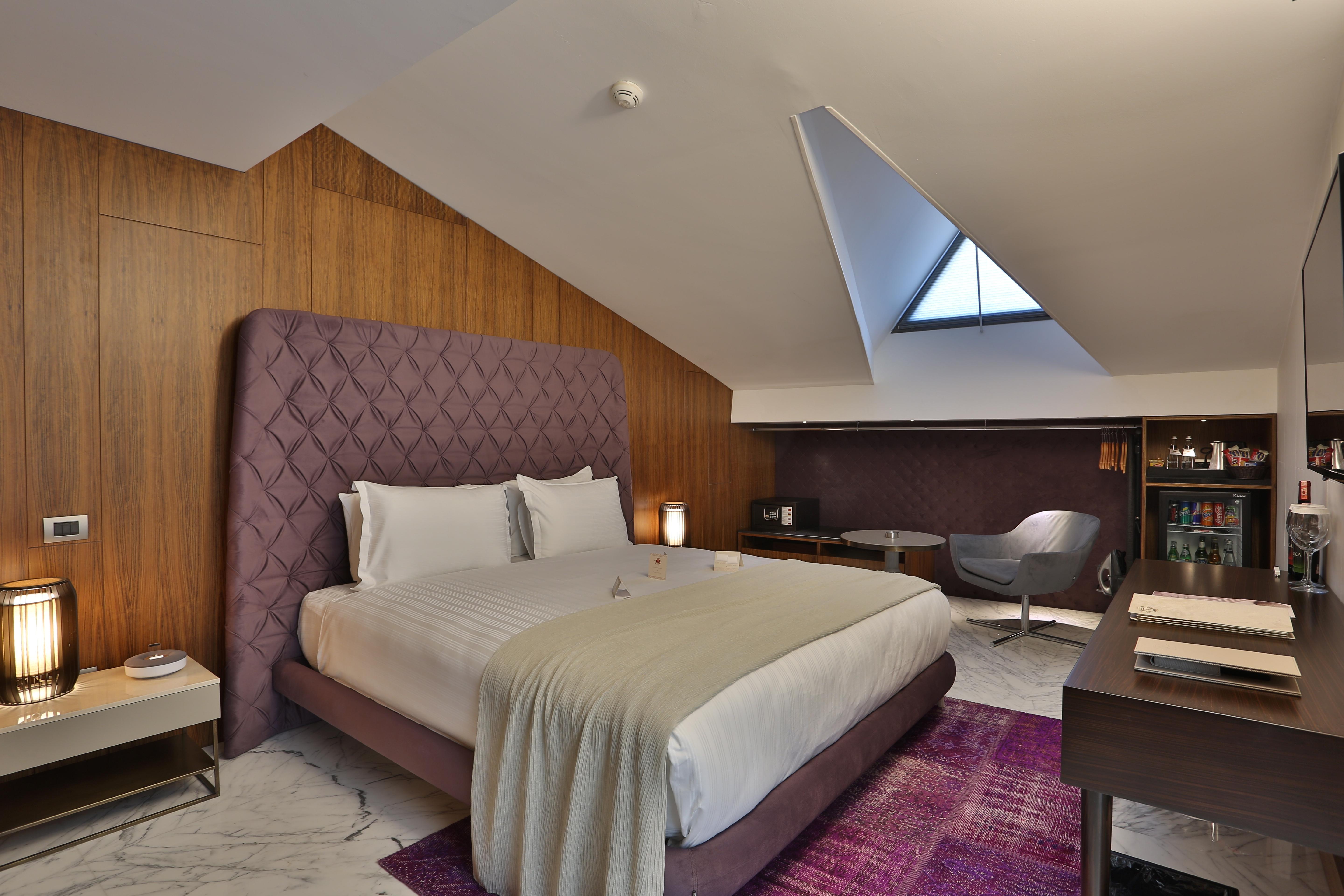 Dosso Dossi Hotels & Spa Downtown Istanbul Ngoại thất bức ảnh The photo shows a stylish hotel room with a modern design. It features a large bed with a tufted purple headboard, complemented by white bedding and a light gray throw. The walls are made of wooden panels, adding warmth to the space. To the side, the