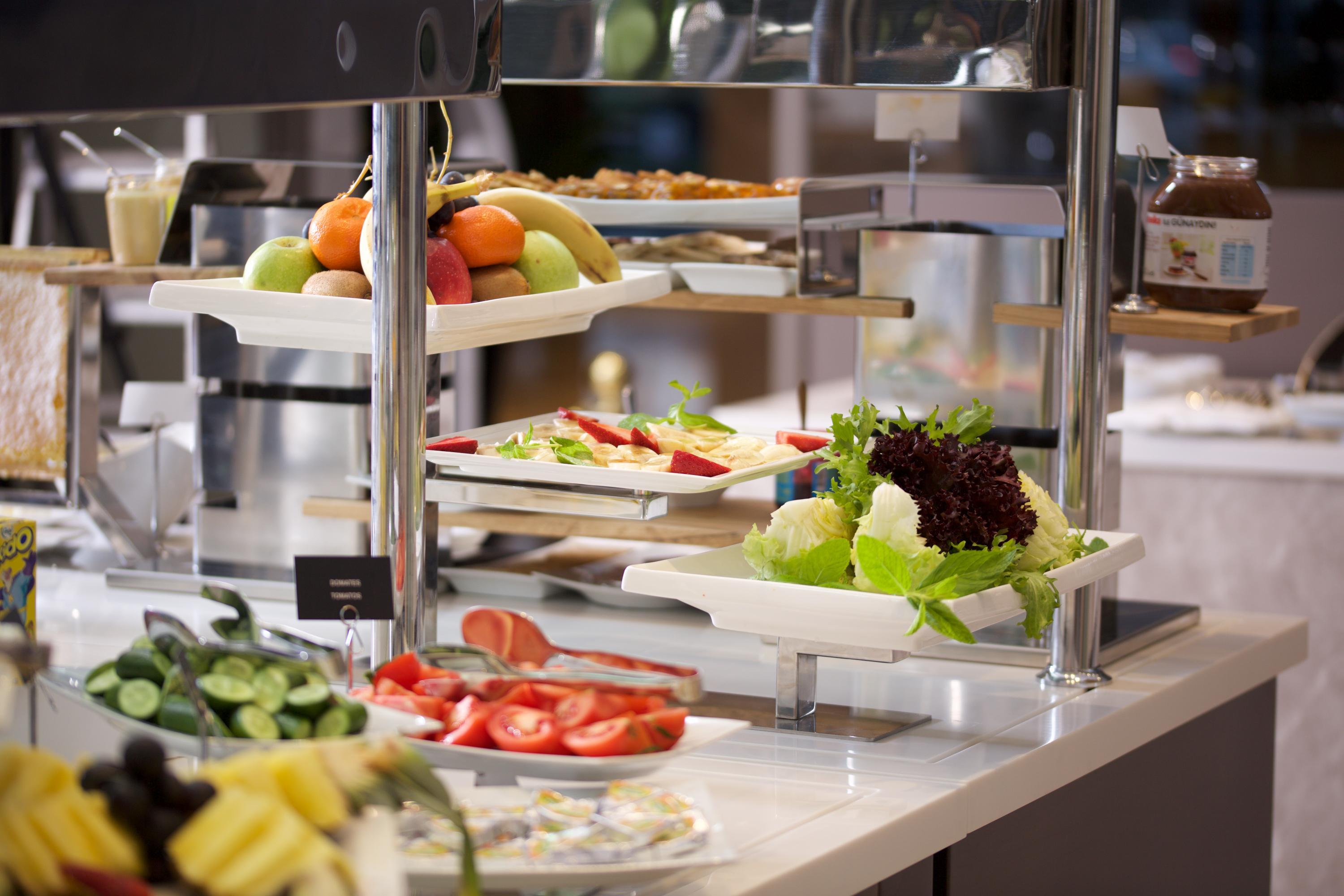 Dosso Dossi Hotels & Spa Downtown Istanbul Ngoại thất bức ảnh The photo depicts a buffet-style setup featuring a variety of fresh food items. There are several trays with colorful fruits, including apples and bananas, positioned on one side. In front, there are plates with vegetables, like sliced tomatoes and l