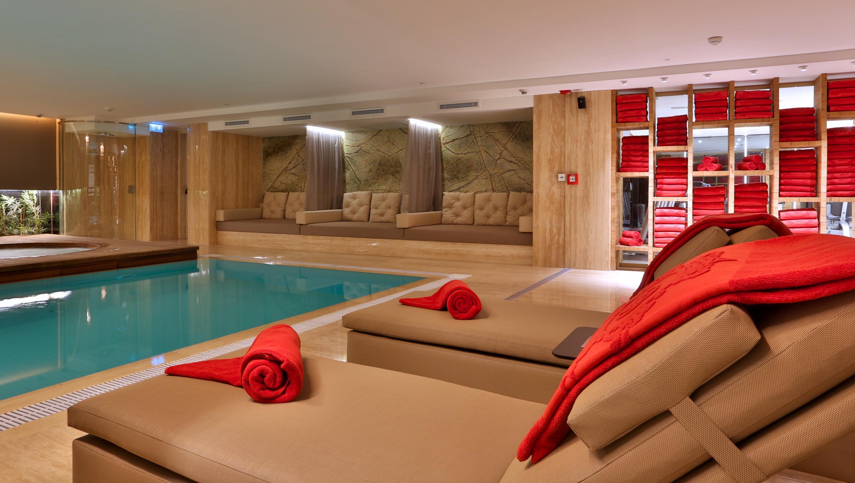 Dosso Dossi Hotels & Spa Downtown Istanbul Ngoại thất bức ảnh The photo shows a modern, luxurious spa area featuring a swimming pool. In the foreground, there are comfortable lounge chairs with red towels rolled and placed on them. The walls are decorated with wood paneling, and there are several plush seating 