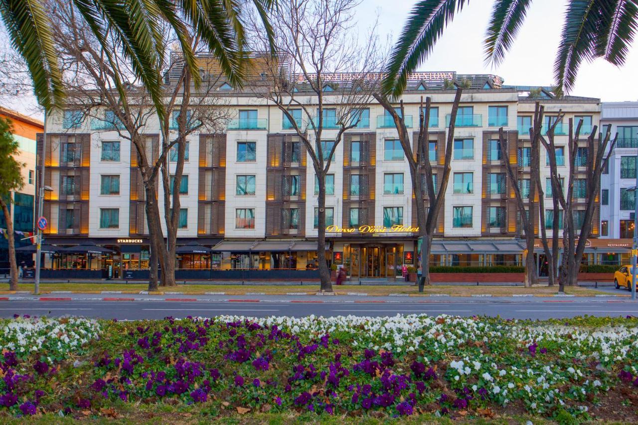 Dosso Dossi Hotels & Spa Downtown Istanbul Ngoại thất bức ảnh The photo shows a building with a modern design, featuring a facade with large windows and a mix of materials. In the foreground, there are colorful flower beds with purple and white flowers. The scene is framed by tall trees, and the overall setting