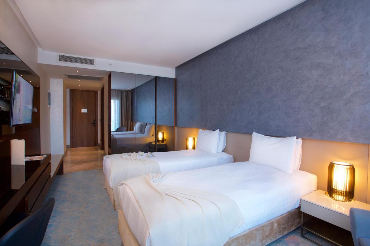 Dosso Dossi Hotels & Spa Downtown Istanbul Ngoại thất bức ảnh The photo shows a modern hotel room featuring two single beds with white bedding. The walls have a stylish gray finish, and there is a decorative element behind the beds. On either side of the beds, there are bedside tables with lamps. A flat-screen 