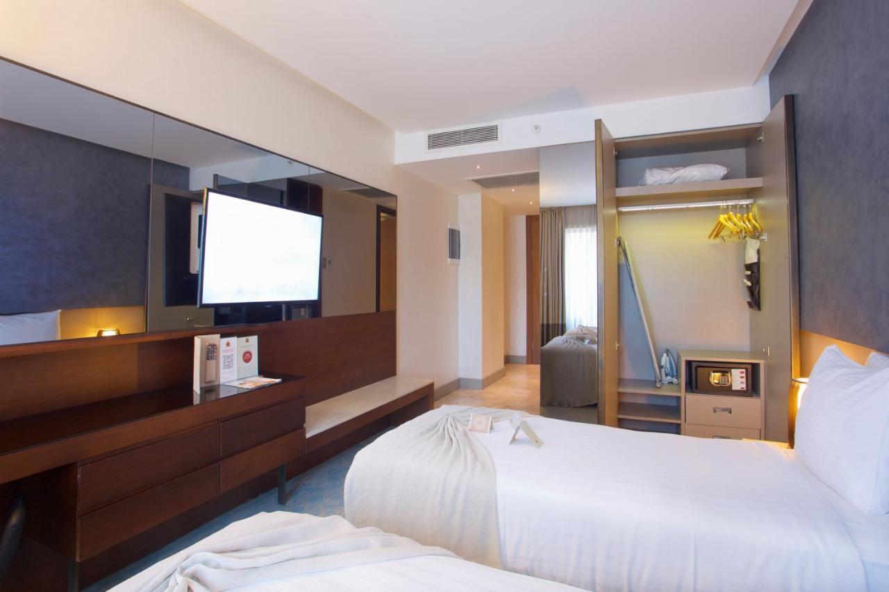 Dosso Dossi Hotels & Spa Downtown Istanbul Ngoại thất bức ảnh The photo shows a modern hotel room featuring two separate beds with white bedding. There's a large flat-screen TV mounted on the wall opposite the beds, and a stylish wooden cabinet beneath it. One corner of the room has an open closet with hanging 