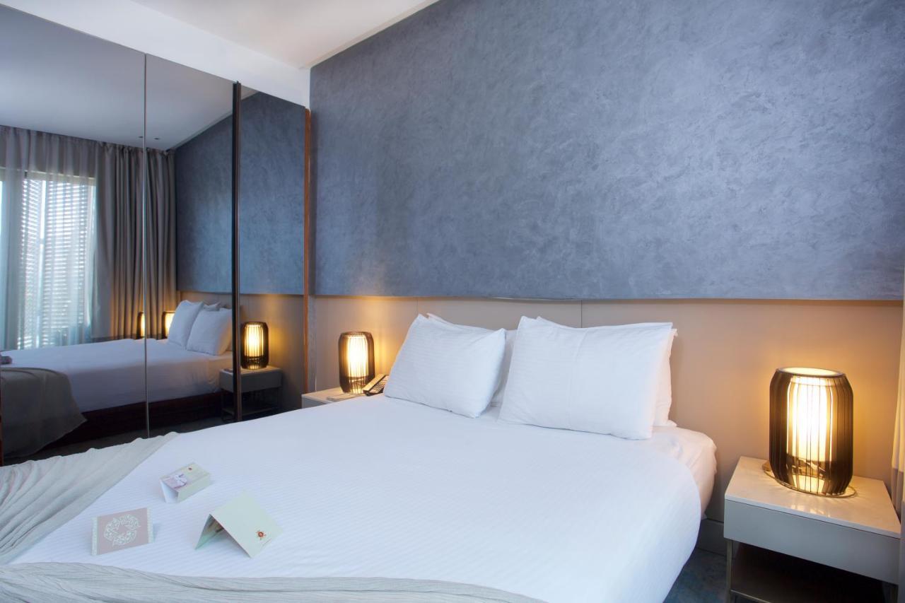 Dosso Dossi Hotels & Spa Downtown Istanbul Ngoại thất bức ảnh The photo depicts a modern hotel room featuring a double bed with white bedding and two pillows. The walls have a smooth, textured finish, and there are large windows with sheer curtains, allowing natural light to filter in. On either side of the bed