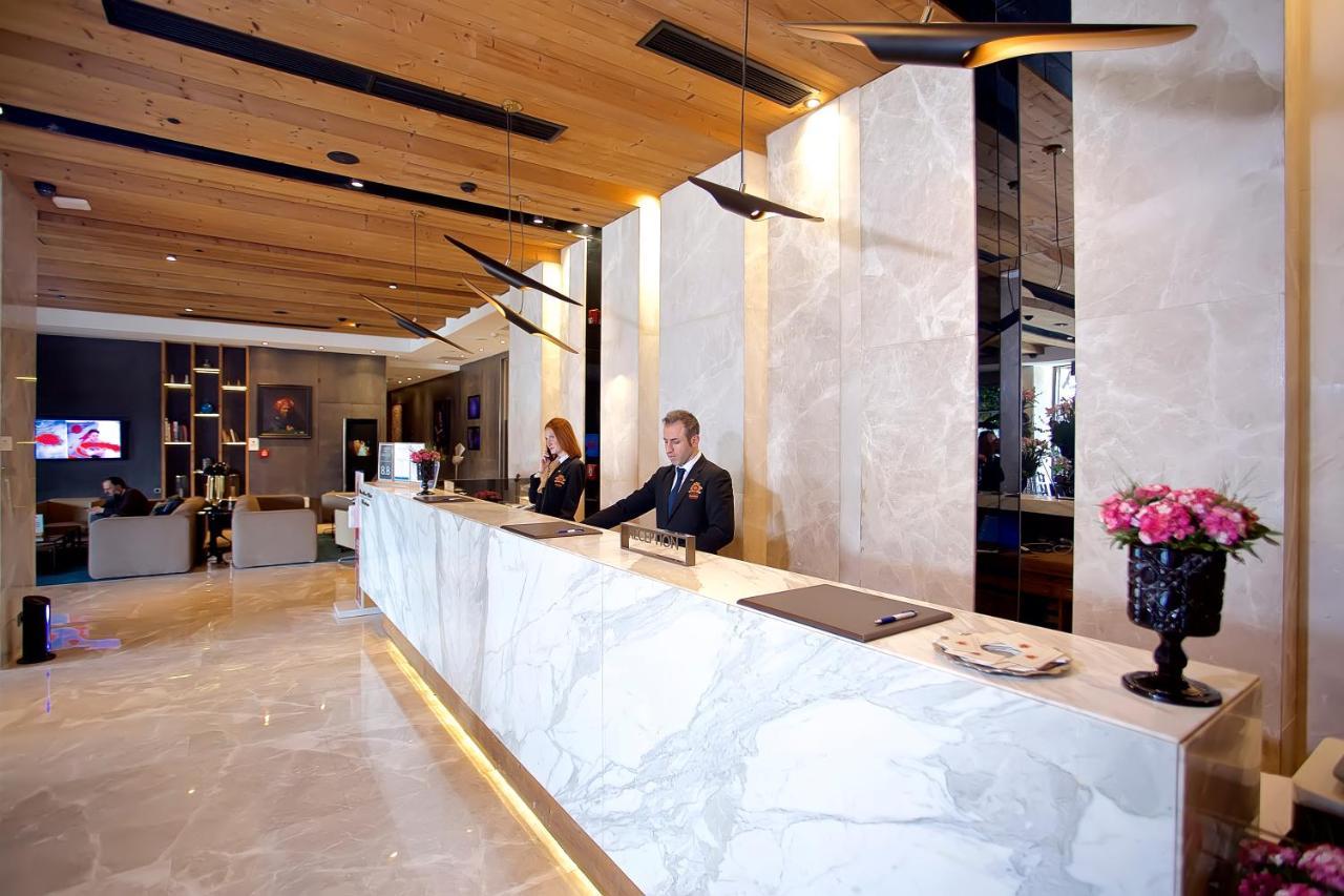 Dosso Dossi Hotels & Spa Downtown Istanbul Ngoại thất bức ảnh The photo shows a hotel lobby reception area. The reception desk is elegantly designed with a marble surface and is situated against a backdrop of light-colored walls. There are two staff members behind the desk—one is a man in a suit, and the other 