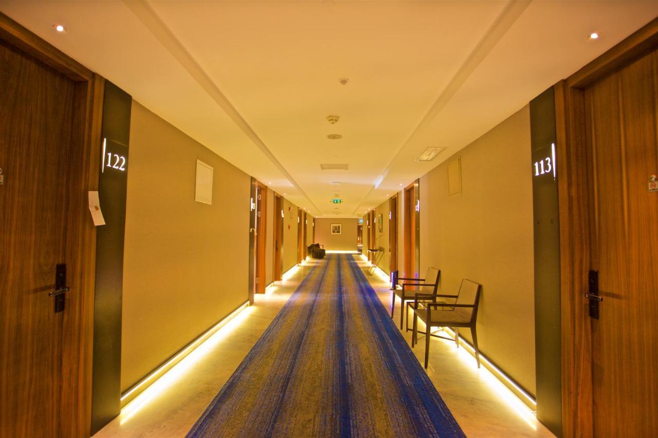 Dosso Dossi Hotels & Spa Downtown Istanbul Ngoại thất bức ảnh The photo shows a hotel corridor with several wooden doors on either side. Each door is numbered, with numbers visible for rooms 113 and 122. The hallway features a long blue rug running down the center and has soft lighting along the sides, creating