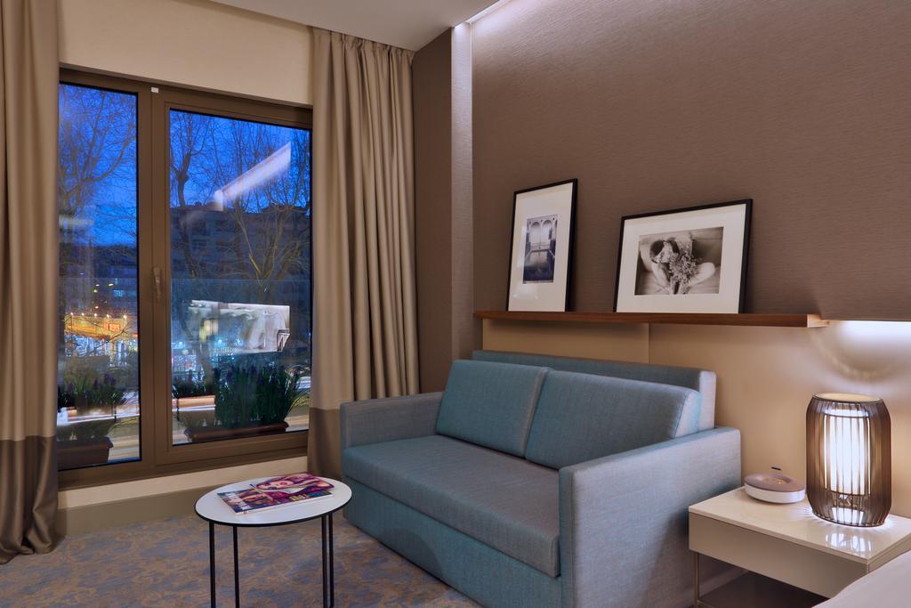 Dosso Dossi Hotels & Spa Downtown Istanbul Ngoại thất bức ảnh The photo shows a modern and cozy interior of a room. There is a light blue sofa positioned against a wall, accompanied by a round coffee table with a magazine on top. Two black-and-white framed photographs are hanging on the wall above the sofa. Lar