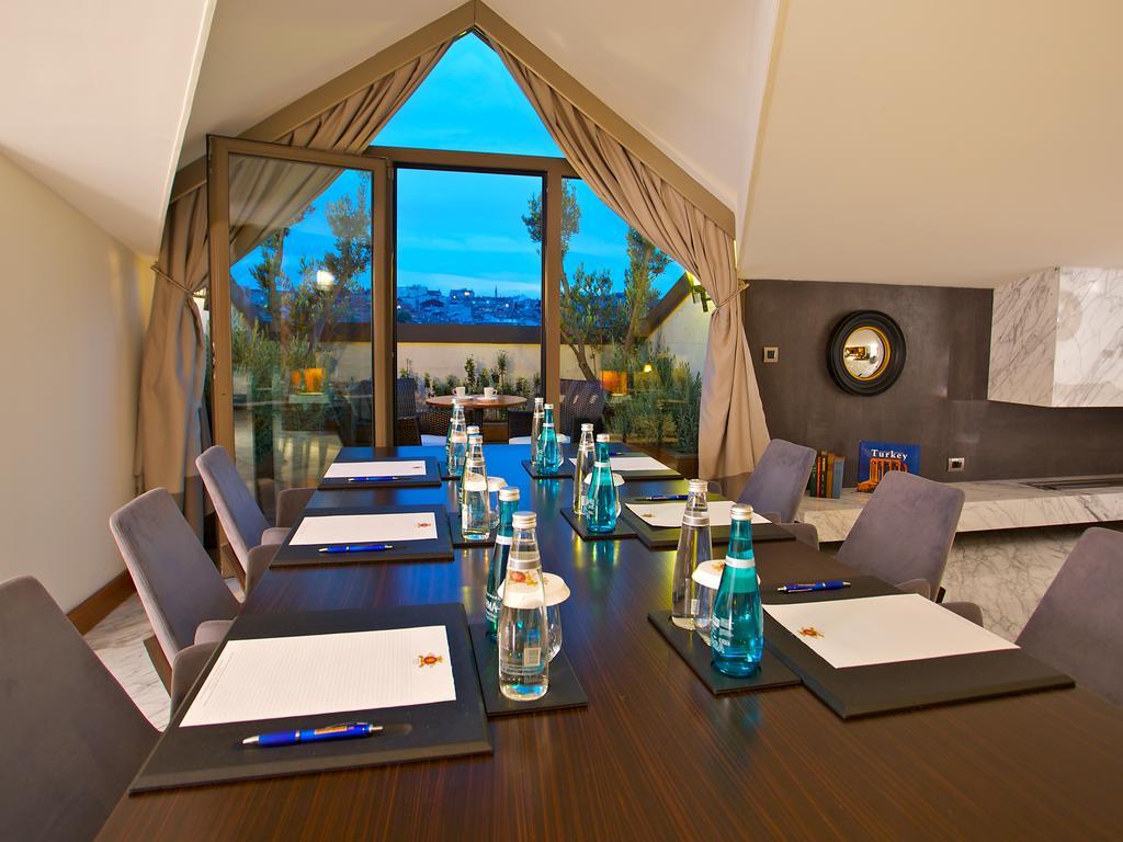 Dosso Dossi Hotels & Spa Downtown Istanbul Ngoại thất bức ảnh The photo shows a conference room setup. There is a long wooden table with several chairs arranged around it. On the table, there are notebooks or notepads, pens, and bottles of water, all placed neatly. The room features large windows with curtains,