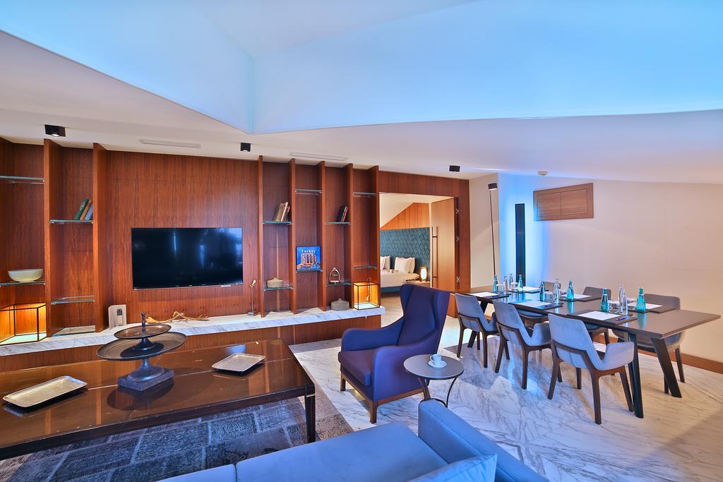 Dosso Dossi Hotels & Spa Downtown Istanbul Ngoại thất bức ảnh The photo shows a modern living space that features an open layout. On the left, there is a comfortable seating area with a sofa and a coffee table. The wall opposite the seating area contains a large flat-screen TV mounted on a stylish wooden panel.