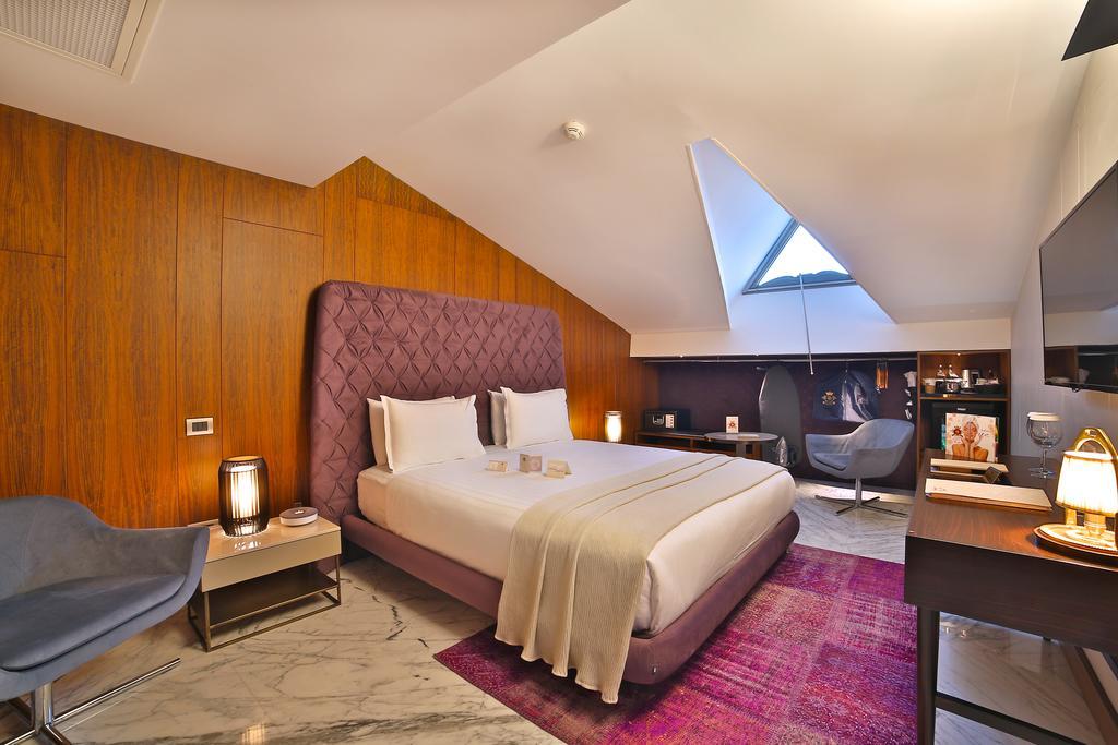 Dosso Dossi Hotels & Spa Downtown Istanbul Ngoại thất bức ảnh The photo shows a modern hotel room featuring a stylish design. It has a large bed with a purple headboard, neatly made with white bedding. The walls are a warm wooden tone, and the room has slanted ceilings with a skylight that lets in natural light