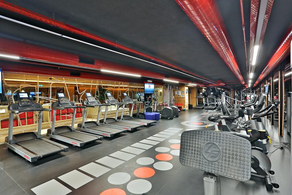 Dosso Dossi Hotels & Spa Downtown Istanbul Ngoại thất bức ảnh The photo shows a modern fitness gym featuring various exercise equipment. On one side, there are several treadmills lined up, facing a screen, likely for entertainment or workout tracking. The flooring has a unique design with colorful circles, and 